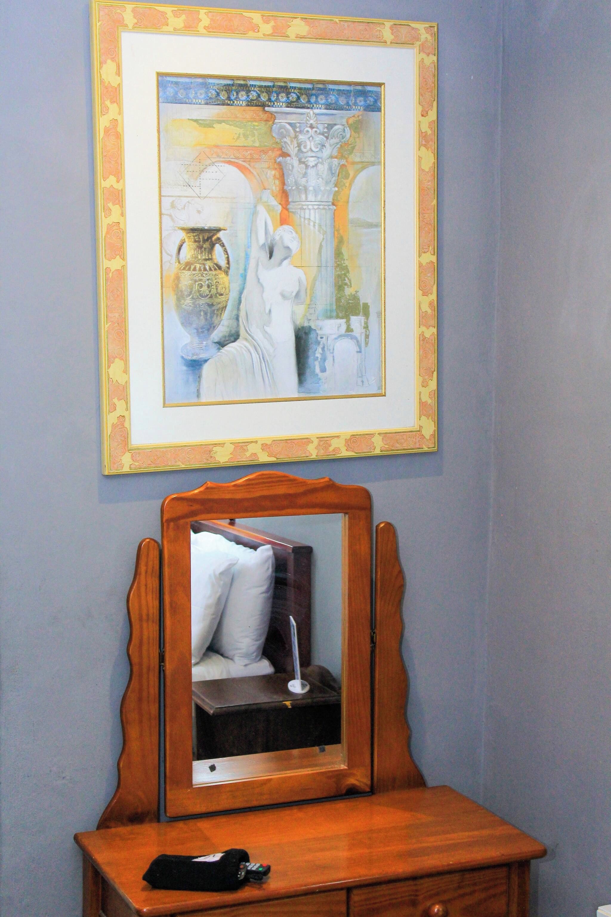 A framed artwork above a wooden dresser with a mirror reflecting part of the room.
