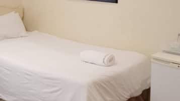 A single bed with a white mattress and pillows, a small bedside table with a white lamp, and a wall-mounted mirror.