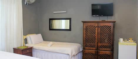 Un dormitorio con cama, armario, televisor y refrigerador pequeño.