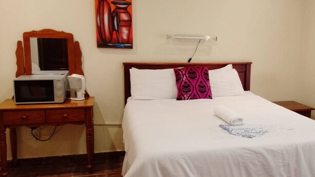 Una habitación de hotel con una cama, una mesita de noche con microondas, una pequeña mesa con tetera y un perchero en la pared.