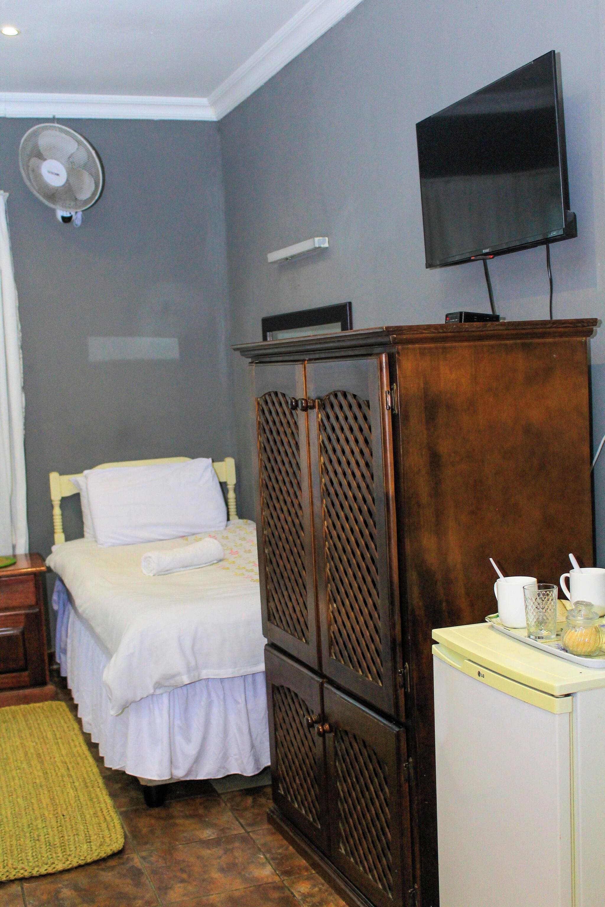 A hotel room with a bed, a wardrobe, a television mounted on the wall, and a small table with a kettle and cups.