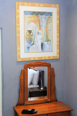 A framed artwork above a wooden dresser with a mirror, a remote control, and a pillow on the dresser.