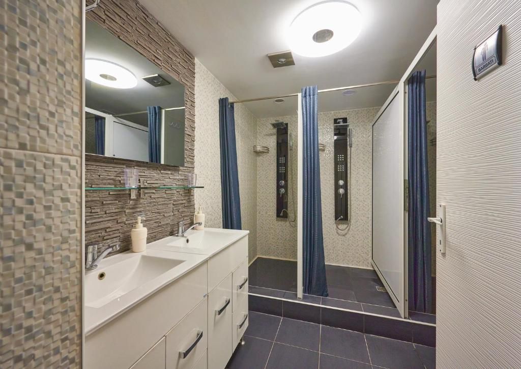 Un baño con espejo, dos lavamanos, ducha e inodoro.