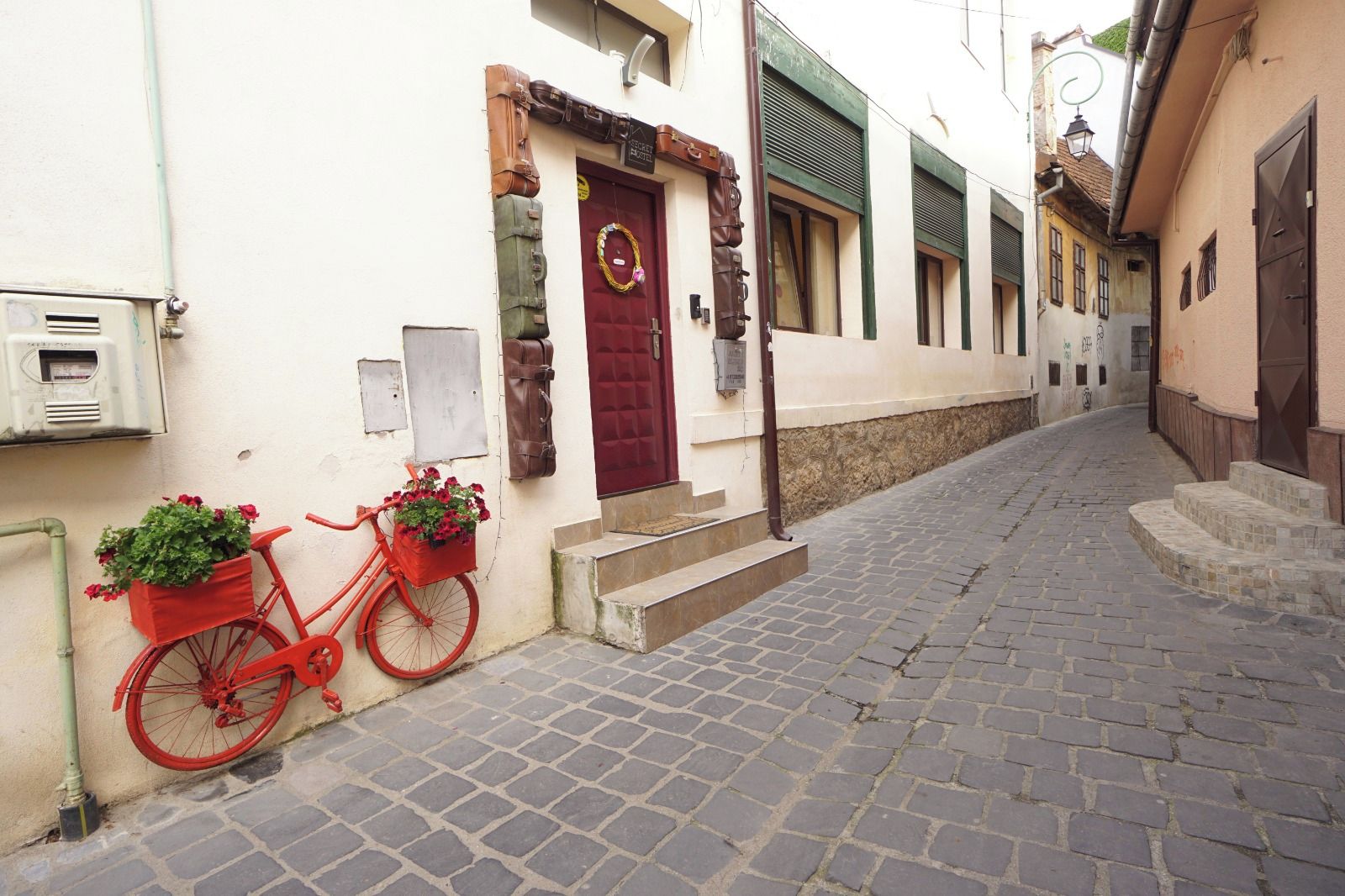 A narrow cobblestone street with a red bicycle parked on the side, a red door, and a mailbox.