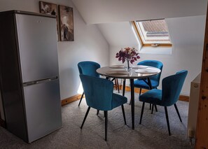 A compact kitchen with a modern refrigerator, a dining table with four blue chairs, and a skylight above. - The Old Print House (Ilkeston)
