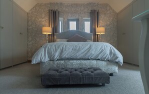 A bedroom with a bed, two bedside lamps, a bench, and a view of the outside through windows. - The Old Print House (Ilkeston)
