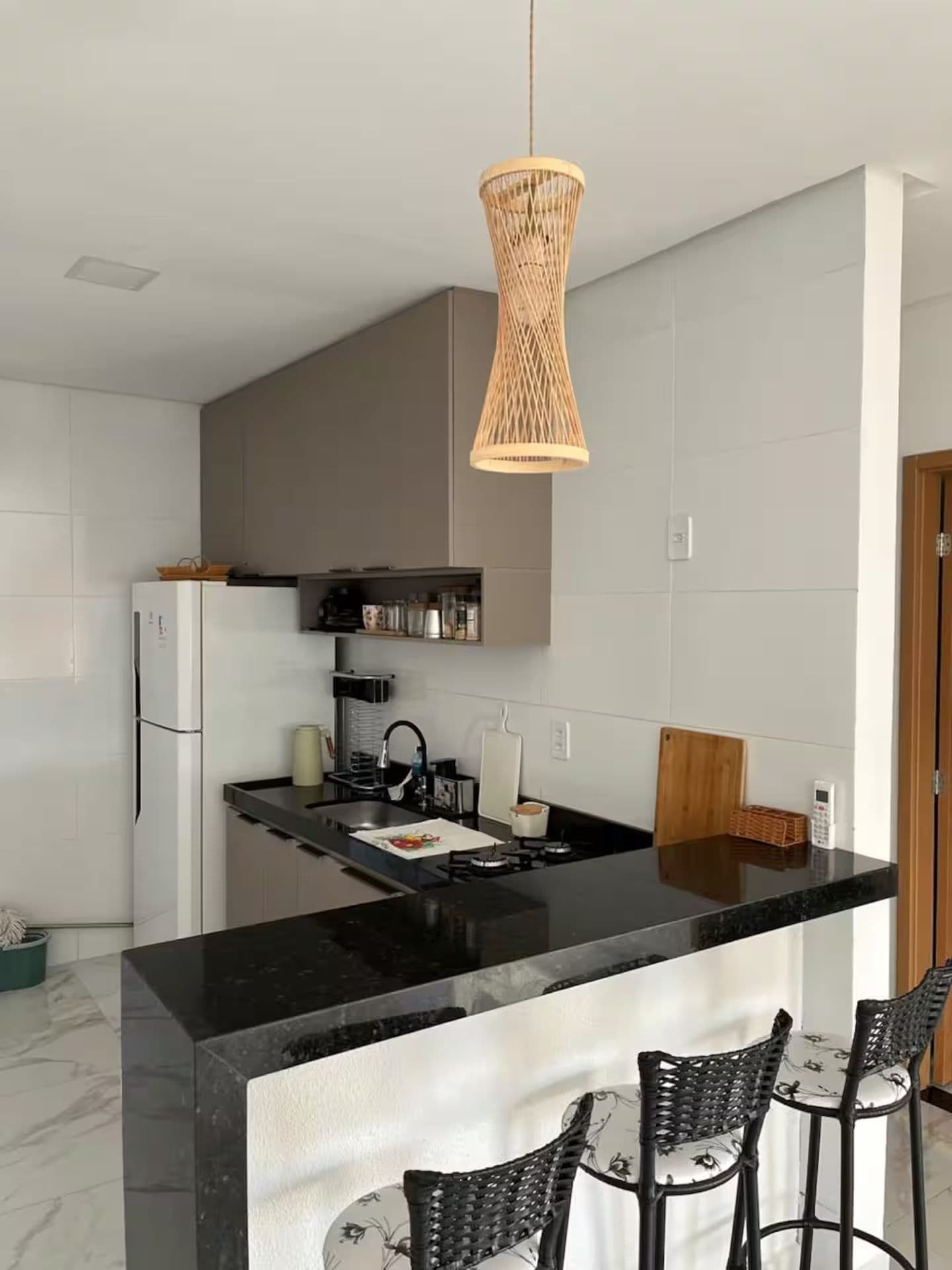 Une cuisine moderne avec un îlot central doté d’un plan de travail noir, un luminaire suspendu en fibres tressées et un coin bar avec des tabourets.