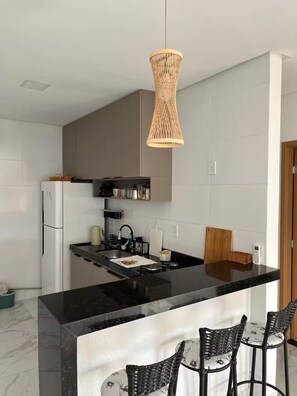 A modern kitchen with a black countertop island, a woven pendant light, and a bar seating area. - Marshal's House / French (Marechal Deodoro)