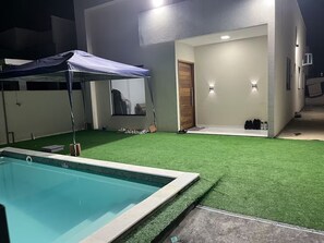 Ein Swimmingpool mit blauer Plane, einem überdachten Bereich, einer Tür und einer Wandleuchte.