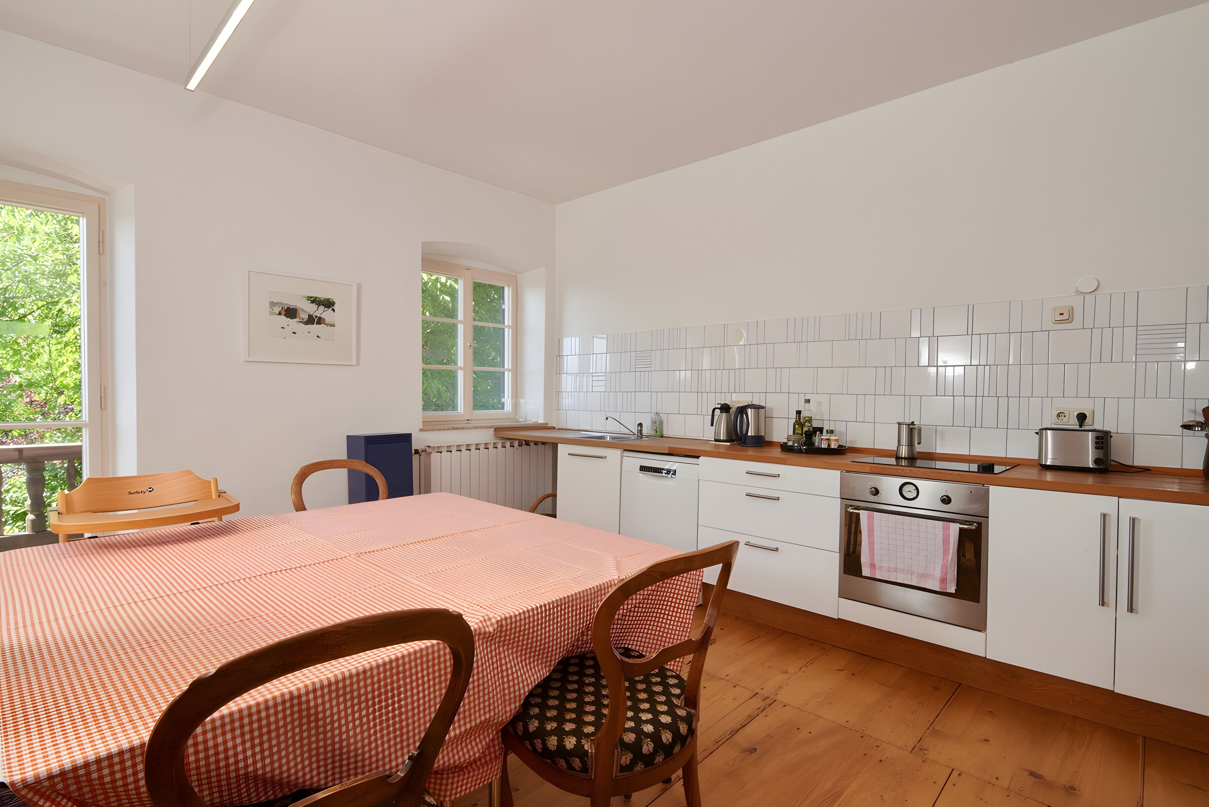 Une cuisine moderne avec des meubles blancs, un plan de travail en bois et une table à manger recouverte d’une nappe à carreaux.