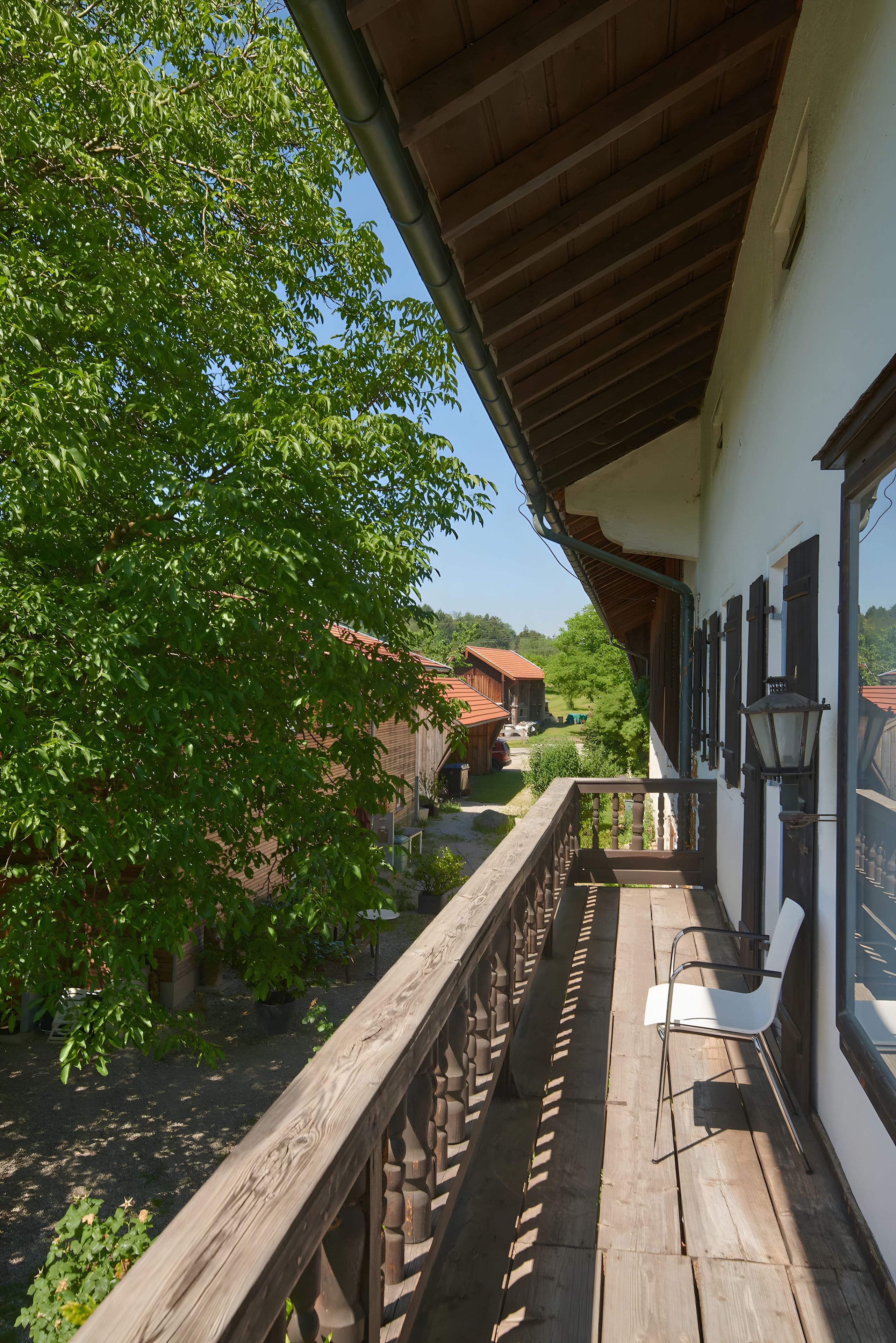 Ein Holzbalkon mit Blick auf einen Baum und ein Gebäude mit rotem Dach.