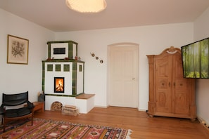 Ein Wohnzimmer mit Kamin, einem schwarzen Ledersessel, einer Holzkommode und einem farbenfrohen Teppich.