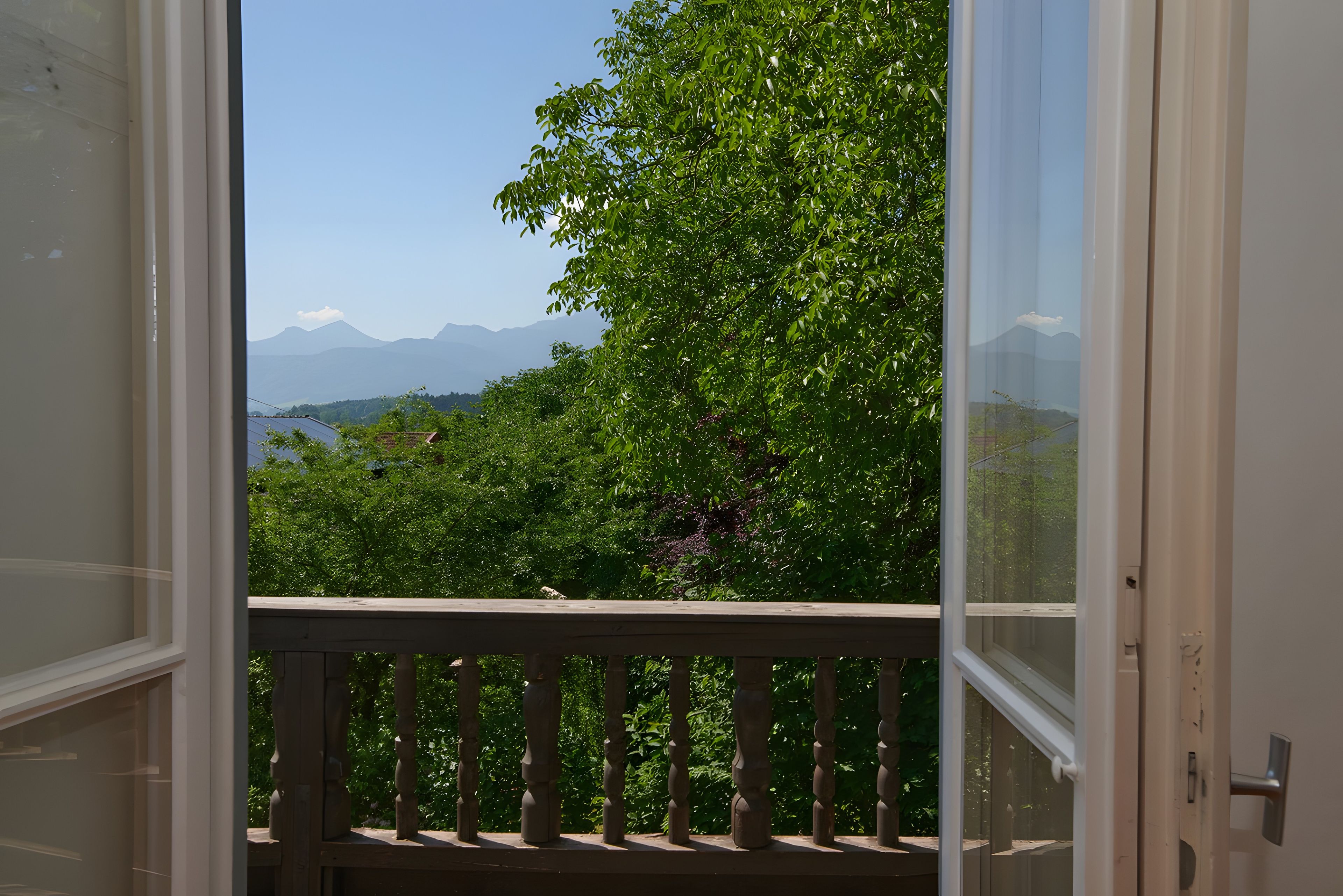 Un balcon doté d’une balustrade en bois, offrant une vue sur un paysage verdoyant et luxuriant ainsi que sur des montagnes lointaines.