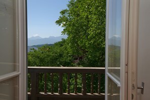Un balcone con ringhiera in legno affaccia su un paesaggio verdeggiante e montagne lontane.