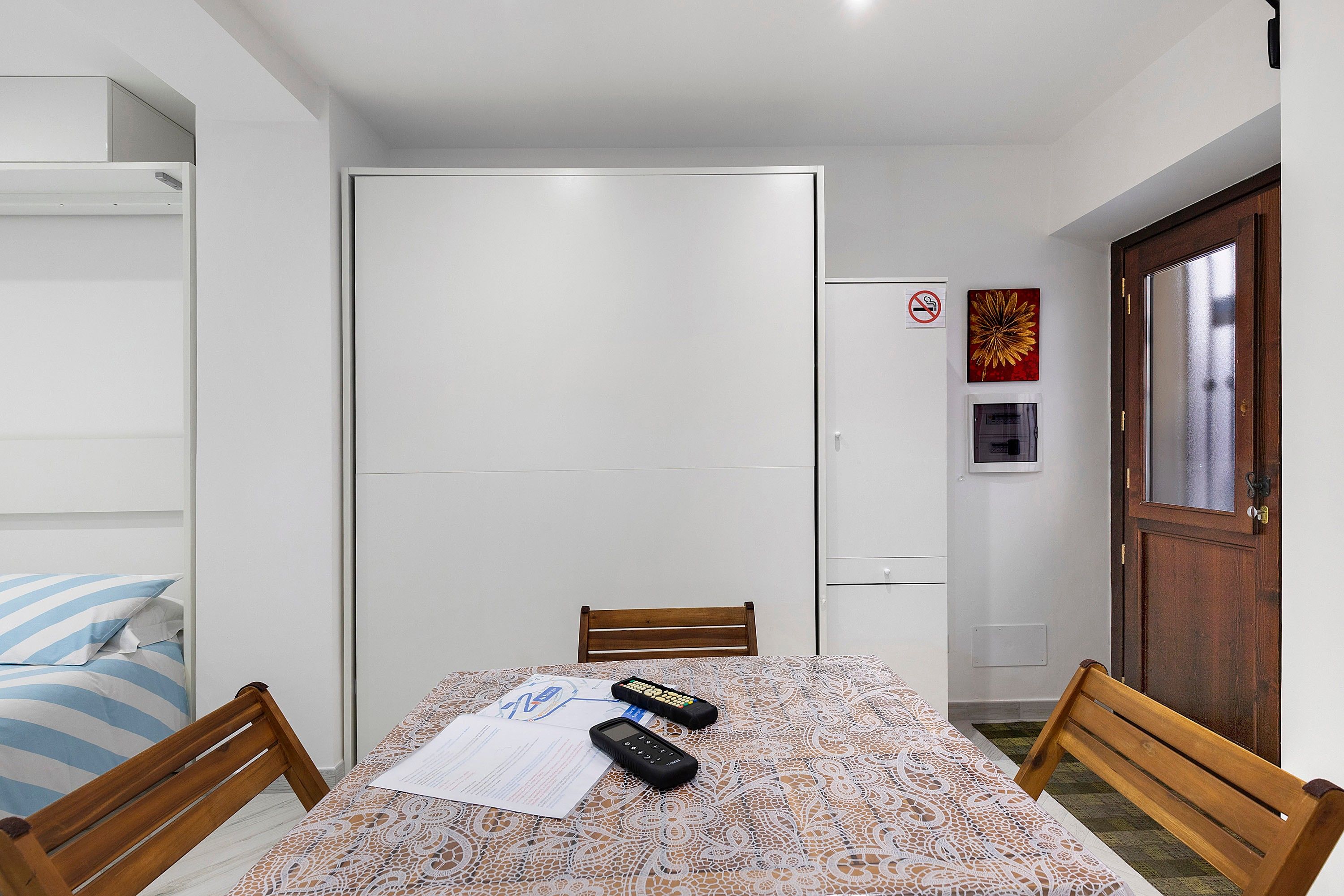 A small room with a bed, a desk, a chair, a wardrobe, and a door.