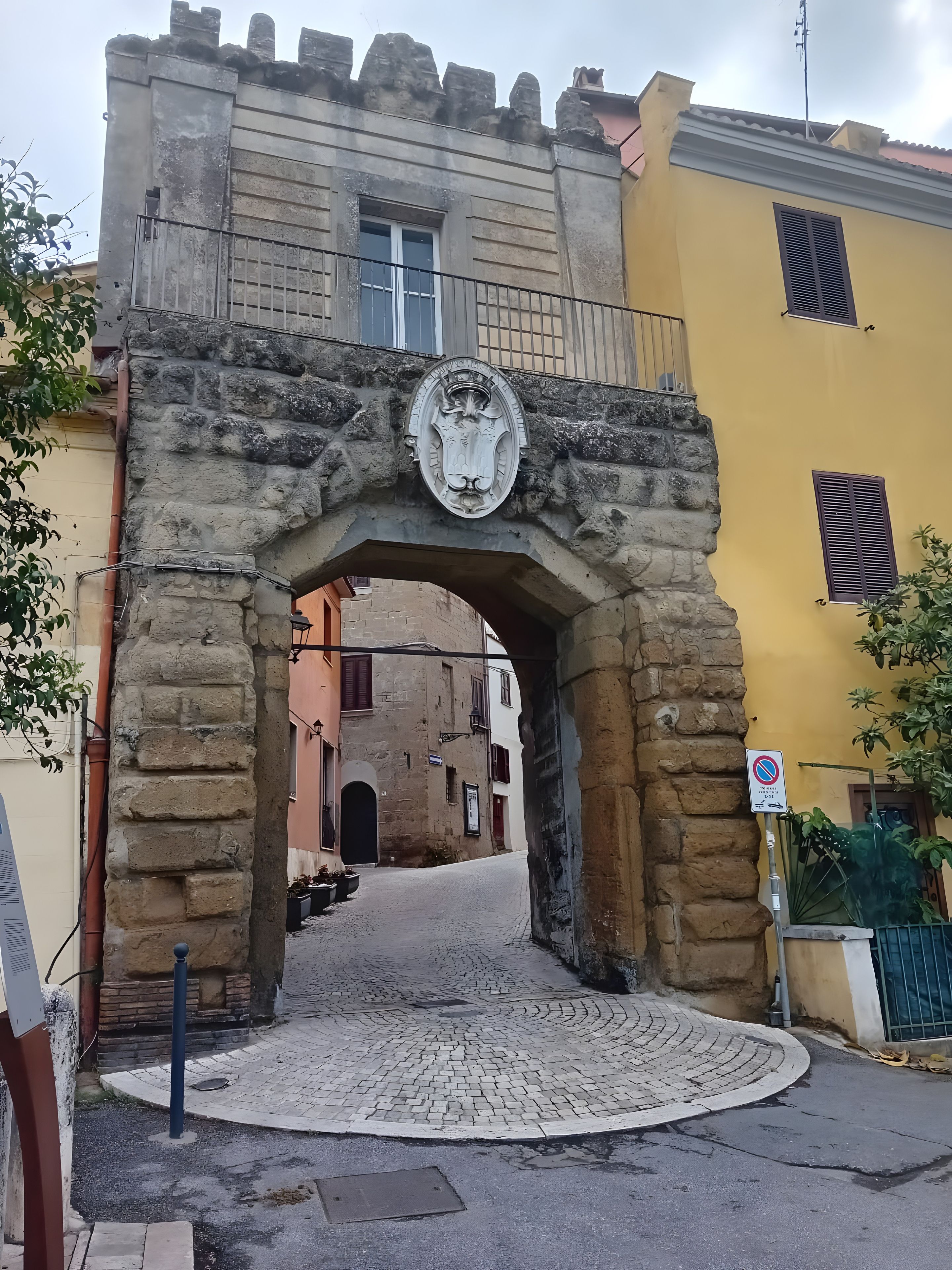 Ein steinernes Tor mit Wappen, das zu einer Kopfsteinpflasterstraße führt.
