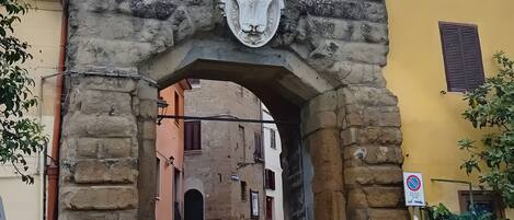 Un arc en pierre orné de blasons, qui mène à une rue pavée.