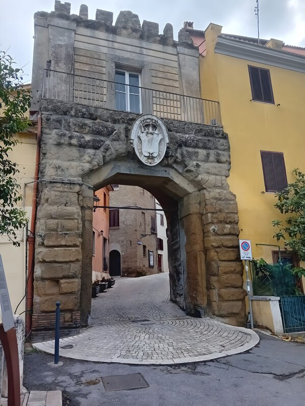 Ein steinernes Tor mit Wappen, das zu einer Kopfsteinpflasterstraße führt.