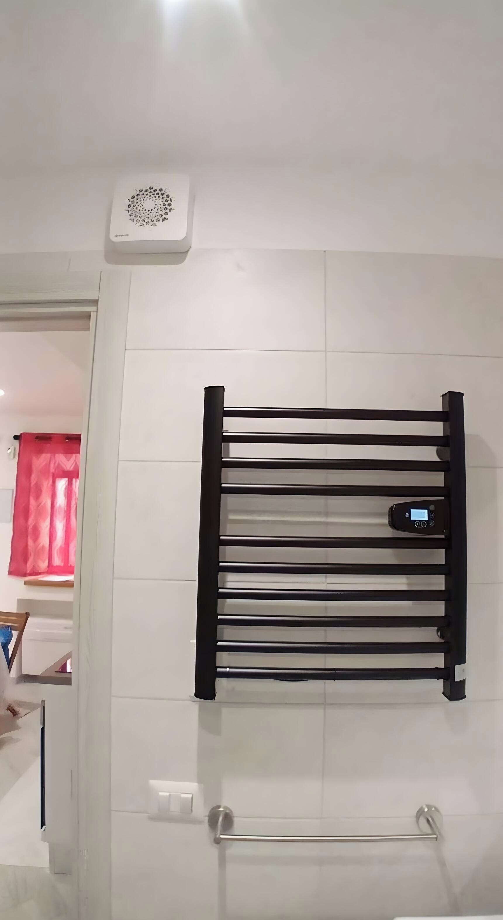 Une salle de bain avec un porte-serviettes noir, un mur blanc et un rideau rouge, dont on ne voit qu'une partie.