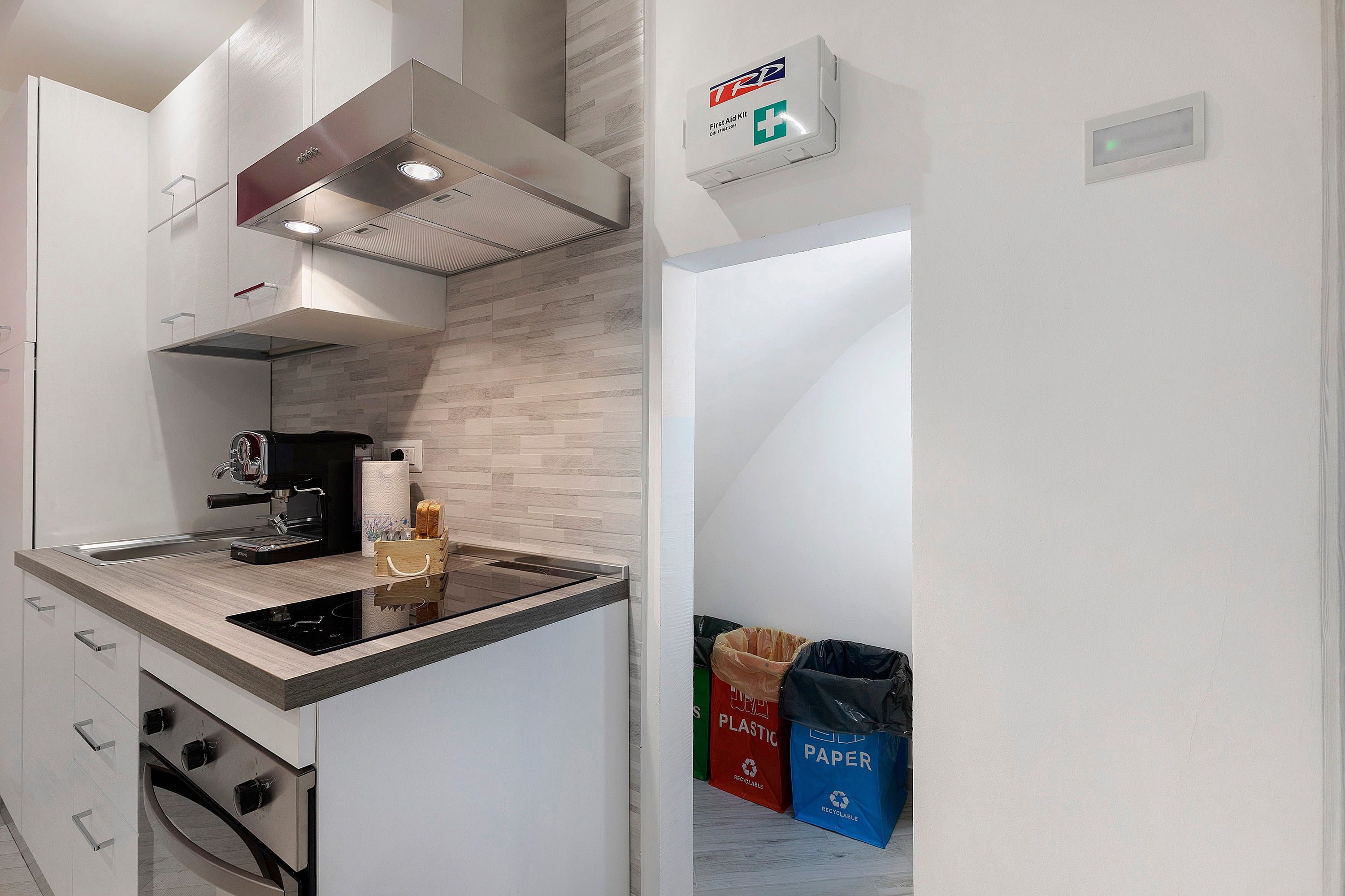 Una cocina moderna con estufa integrada, máquina de café y un botiquín de primeros auxilios en la pared.