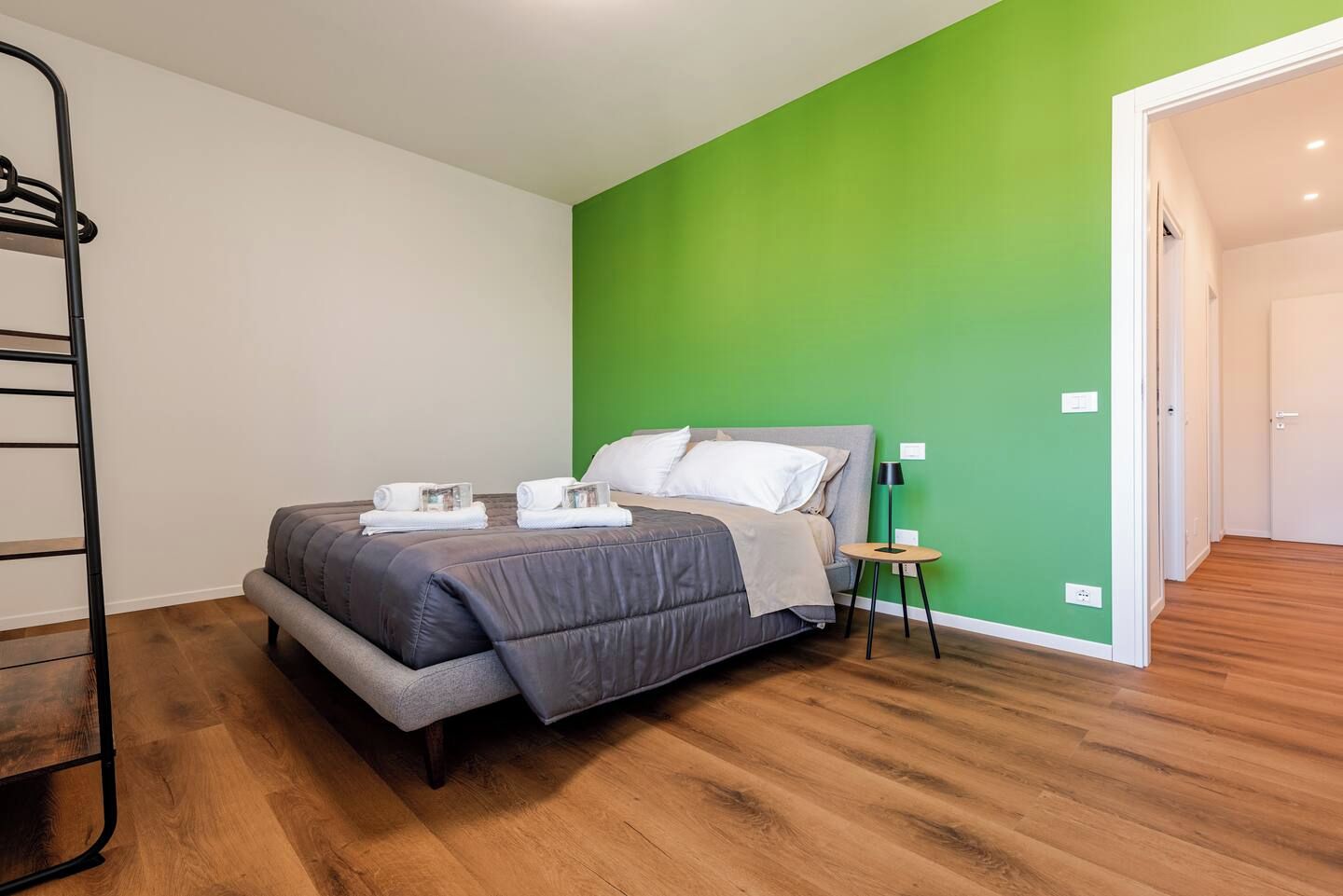Une chambre à coucher avec un lit, une table de chevet, un mur vert et un plancher en bois.