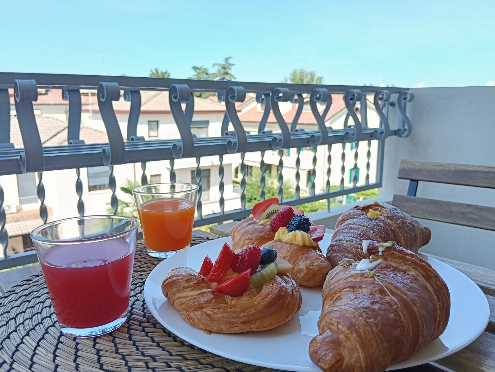 Un balcone con un tavolo apparecchiato per la colazione, con croissant, frutta e un bicchiere di succo d'arancia.