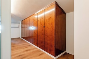 Quarto com guarda-roupa de madeira, paredes brancas e chão de madeira.
