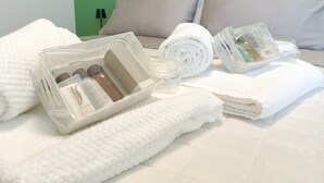 A neatly made bed with white linens, a rolled towel, and a clear plastic container with toiletries. - [Padova] Attico Deluxe 150 mq - Nuovo 2025 (Padova)