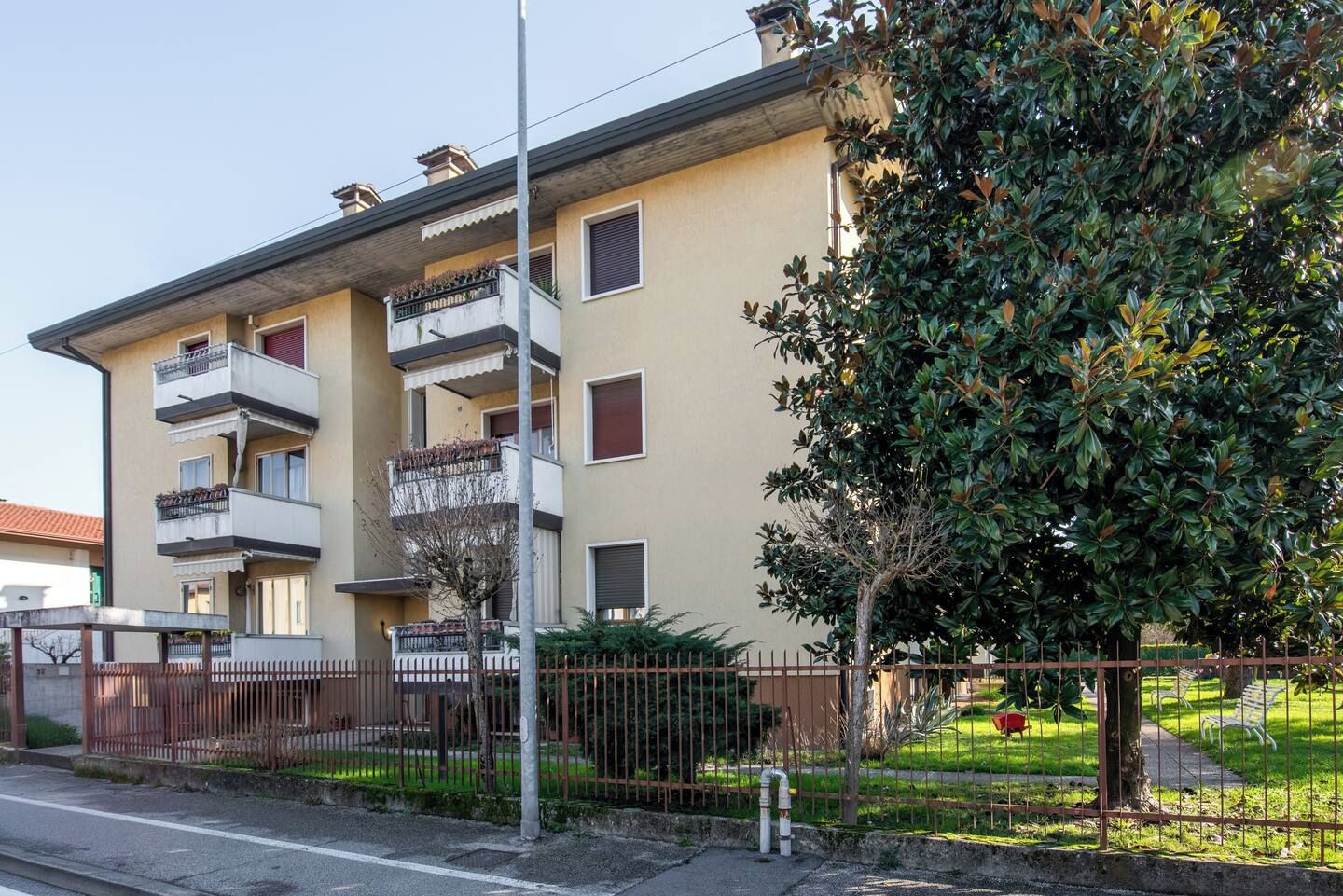 Un edificio residenziale a più piani con balconi, un ingresso carrabile e un prato curato.
