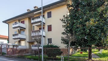 Un edificio residenziale a più piani con balconi, un ingresso carrabile e un prato curato.