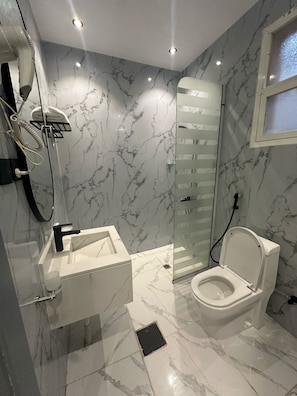 Een moderne badkamer met een marmeren vloer, een wit toilet, een douchecabine van glas en een wit wastafelmeubel met een zwarte kraan.