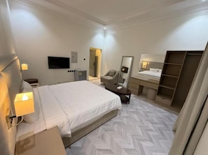 Een hotelkamer met een bed, nachtkastje, stoel, bureau, spiegel, kledingkast en een televisie.