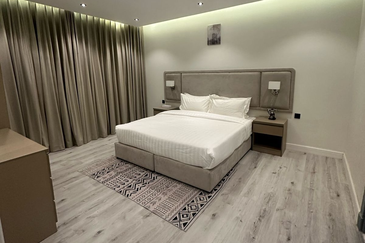 Een moderne slaapkamer met een groot bed, bedlampen, een nachtkastje en een kamerkleed met dessin.