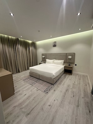 A modern bedroom with a large bed, bedside lamps, a nightstand, and a patterned rug.
