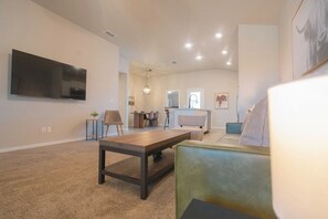 A modern living room with a large flat-screen TV, a wooden coffee table, and a green sofa. - The Winsome Western - HotTub - Fire Pit - PingPong (Lubbock)