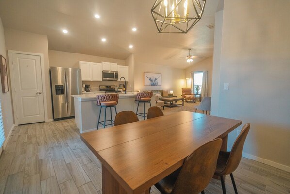 Una cocina moderna con electrodomésticos de acero inoxidable, un comedor con mesa y sillas de madera, y una sala de estar con sofá y mesa de centro.