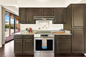 A kitchen with dark wood cabinets, a stainless steel range, and a granite countertop. - Desert Escape with Mountain Views (Oro Valley)