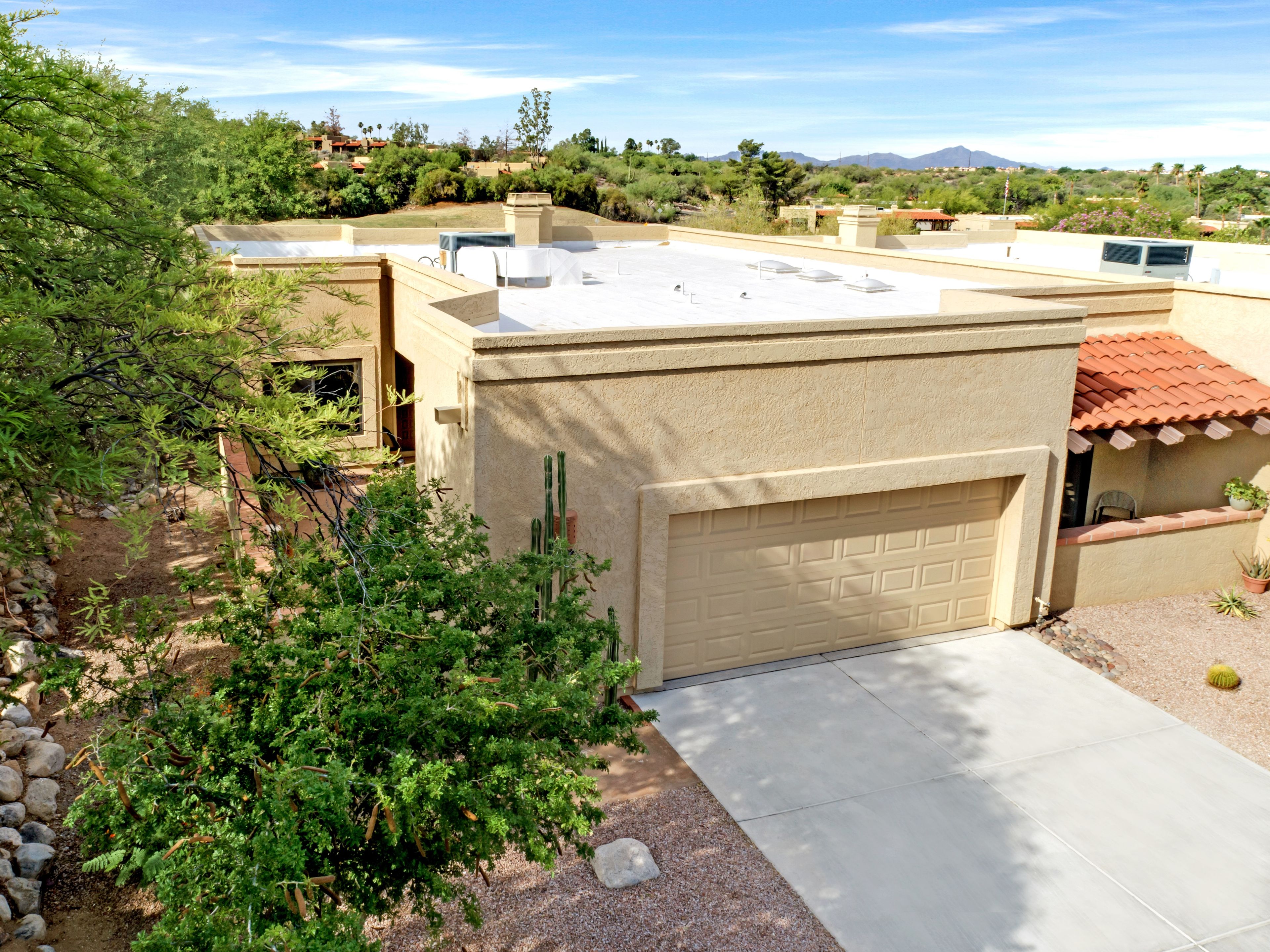 A residential building with a flat roof, a garage, and a garden area with various plants.