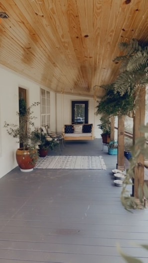 A covered porch with a wooden ceiling, a bench, and potted plants.