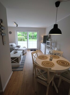 A modern living space with a dining area, a sofa set, a television, and a view through a glass door. - Holiday Home With 1 Bedroom (St. Peter-Ording)