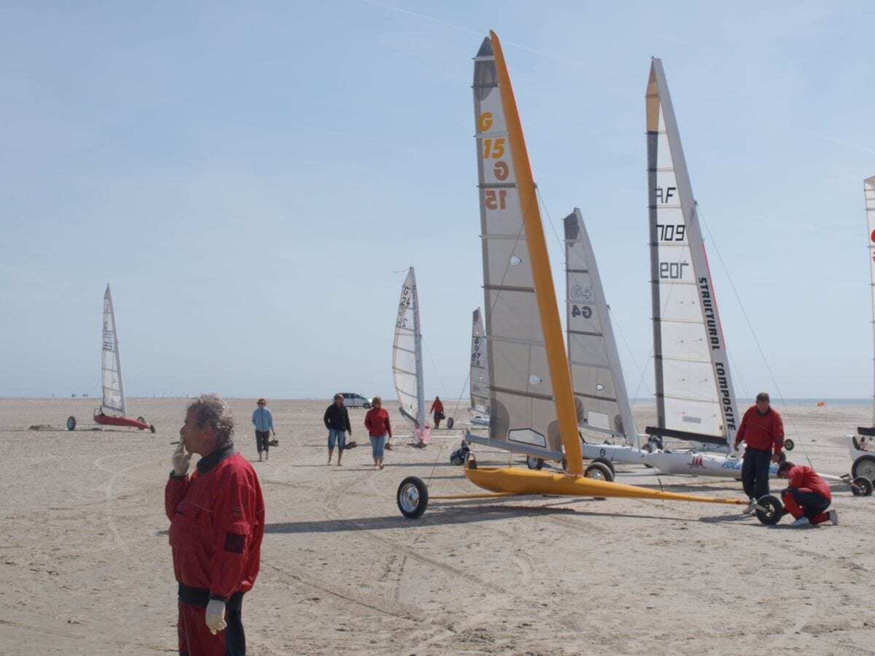 A beach with multiple windsurfing boards and people in red jackets.