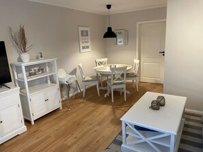 A room with a dining table, chairs, a white cabinet, a television, and a door. - Holiday Home With 1 Bedroom (St. Peter-Ording)