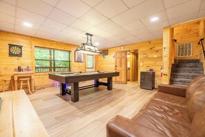A wooden interior with a pool table, a sofa, and a staircase. - Country Bear Cove: Cozy Pigeon Forge Cabin with Hot Tub & Game Room (Pigeon Forge)