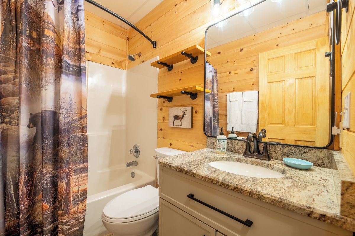 A bathroom with a shower, toilet, sink, and a mirror.