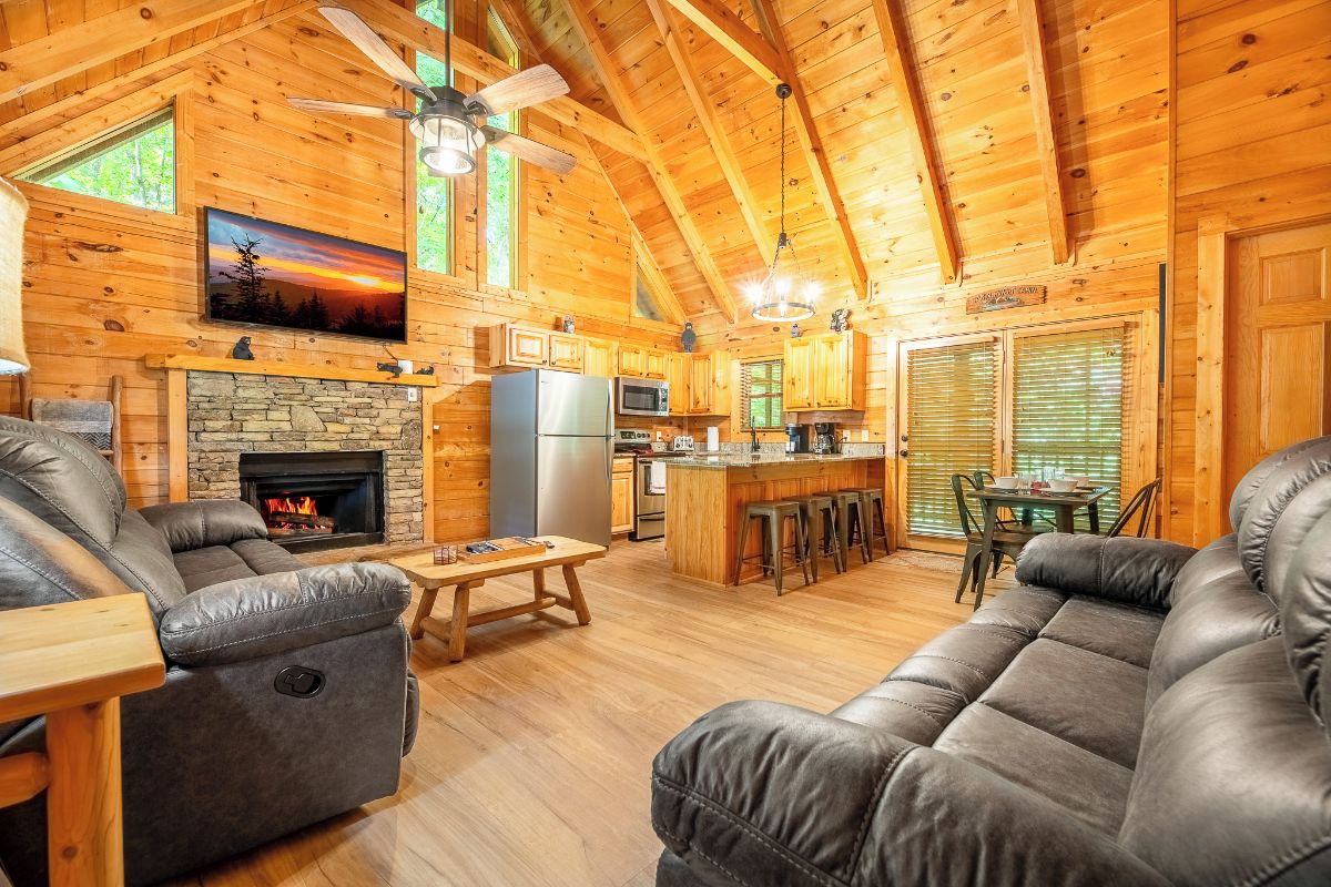 A log cabin interior with a fireplace, a dining area, and a kitchen.