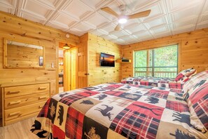 A wooden cabin bedroom with a bed, a dresser, a television, and a window with blinds. - Country Bear Cove: Cozy Pigeon Forge Cabin with Hot Tub & Game Room (Pigeon Forge)