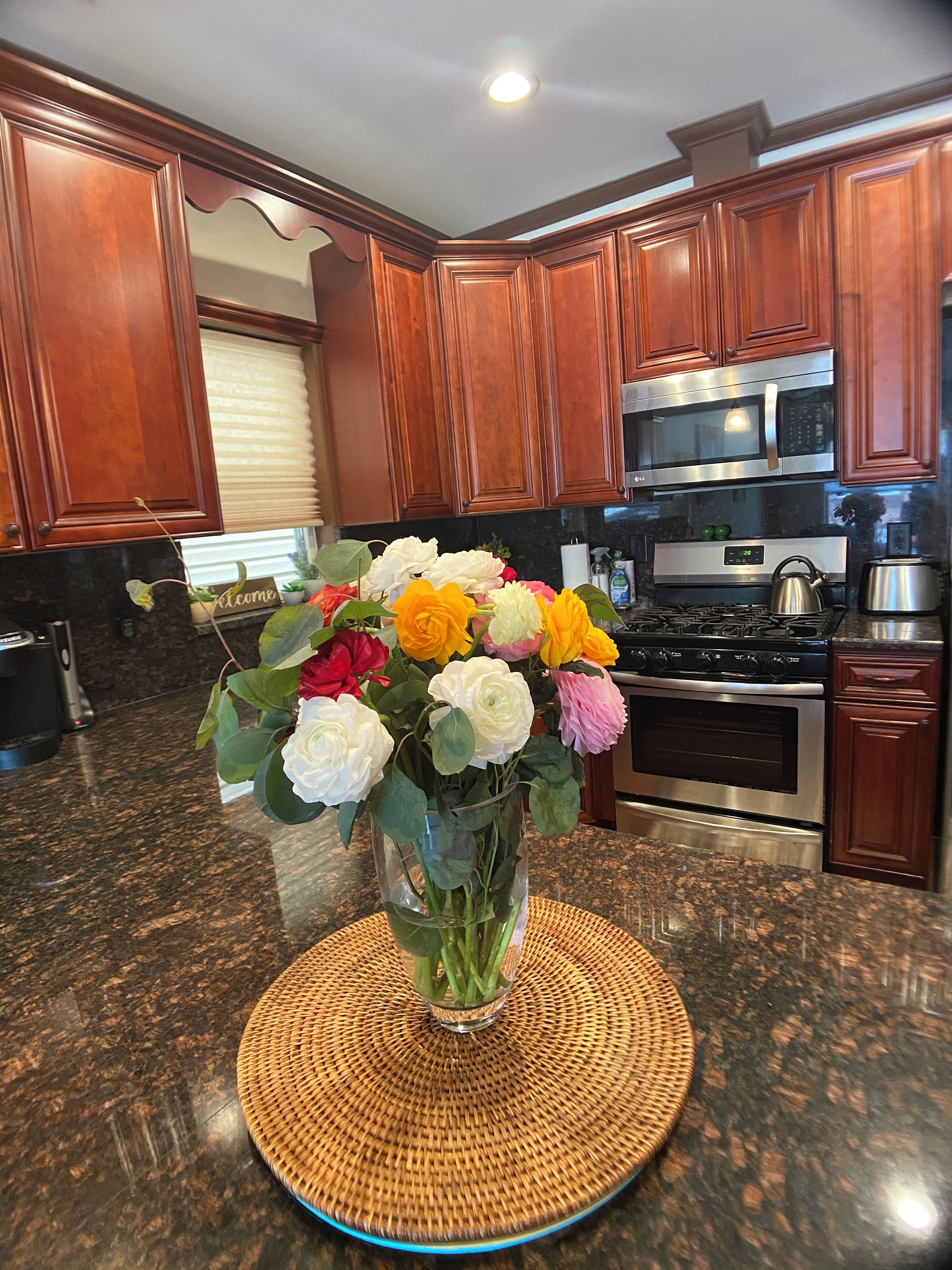 A kitchen with wooden cabinets, a microwave, a stove, and a vase of flowers on the counter.