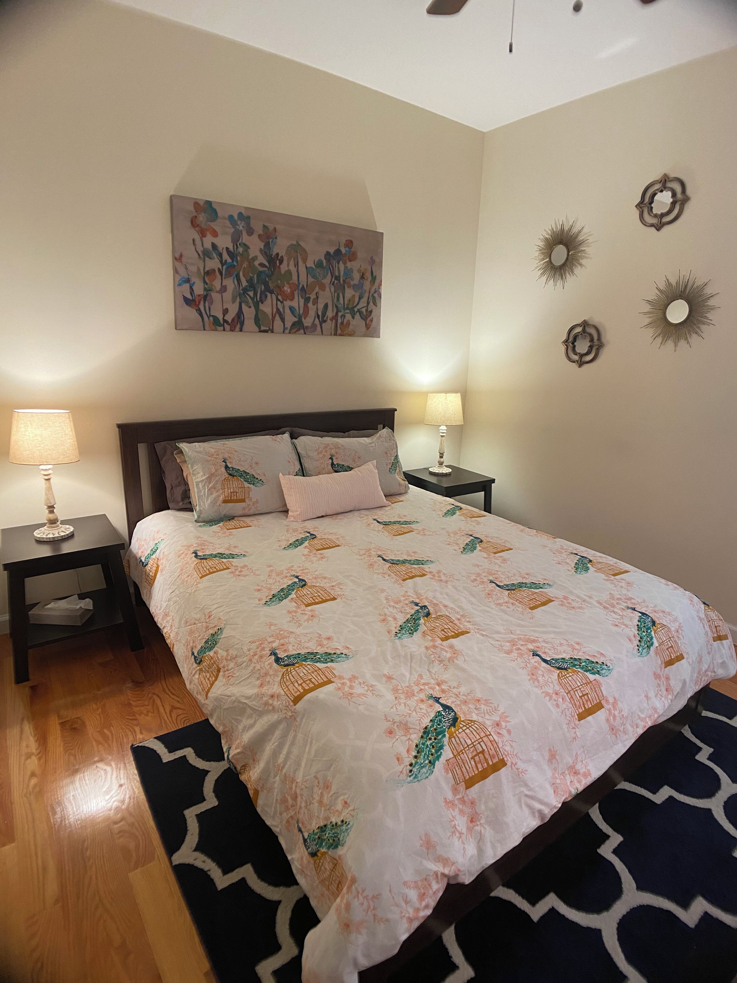 A bedroom with a bed, two bedside tables, a wall-mounted artwork, and decorative wall sconces.