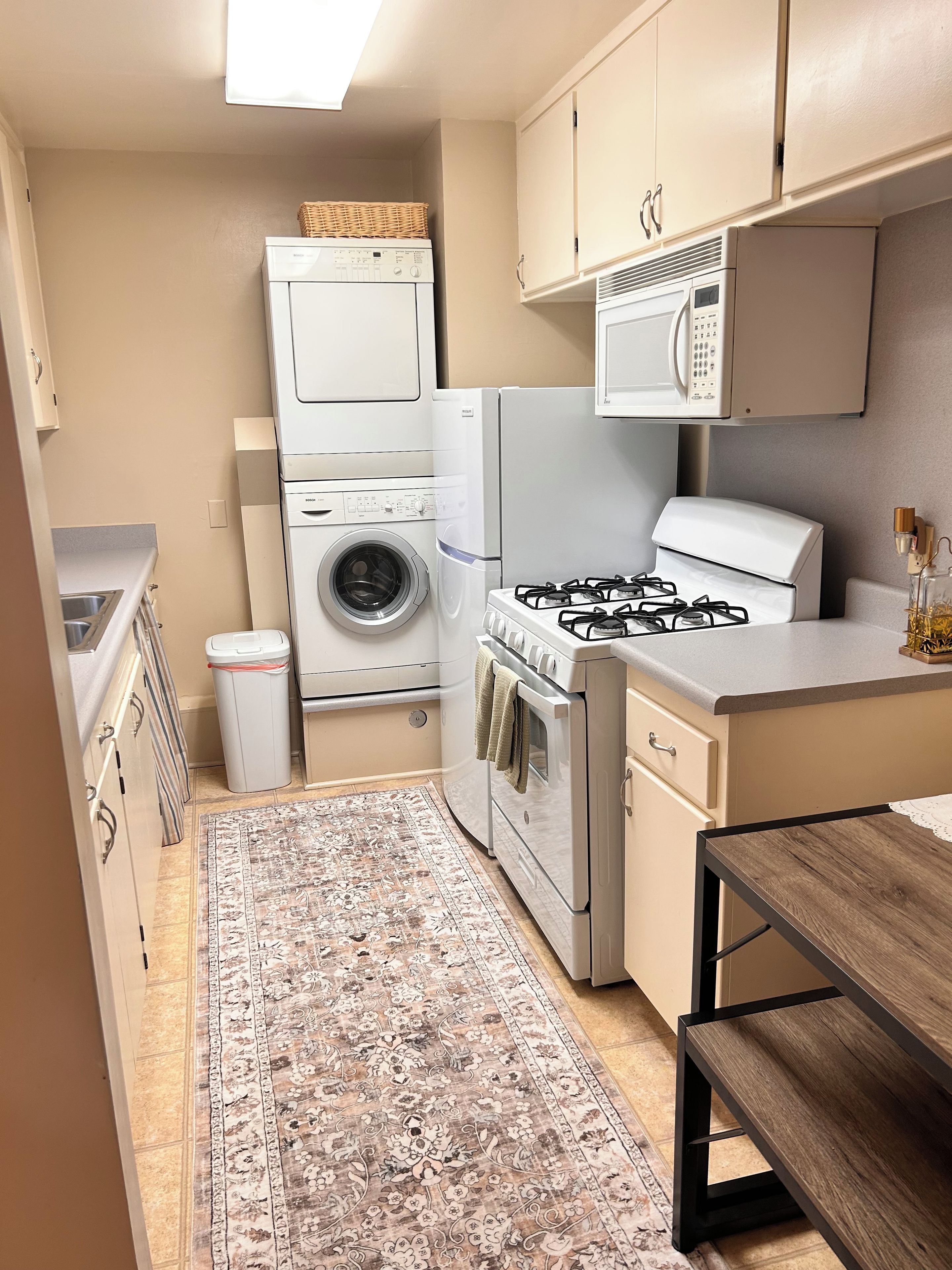 Cozinha compacta com máquina de lavar, micro-ondas, fogão a gás e um pequeno espaço de refeições.