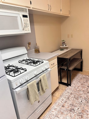Una cocina con estufa blanca, microondas y una pequeña mesa con una planta.